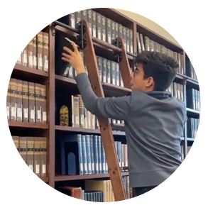 Carols climbs the library ladder to get a research book from the top shelf